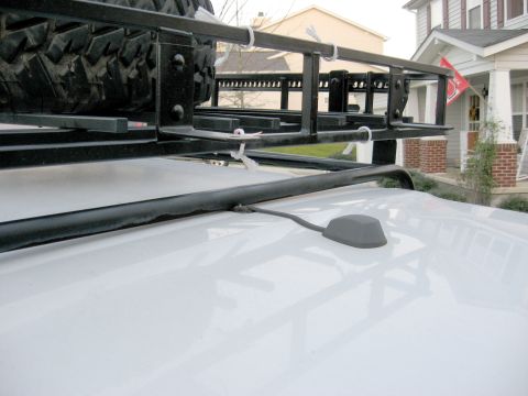 1996 Ford Bronco - A white vehicle's roof is visible, equipped with a black roof rack and a spare tire, along with a gray antenna.
