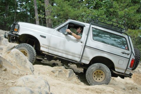 1996 Ford Bronco - Driver maneuvers a white 1996 Ford Bronco over a challenging rock obstacle.