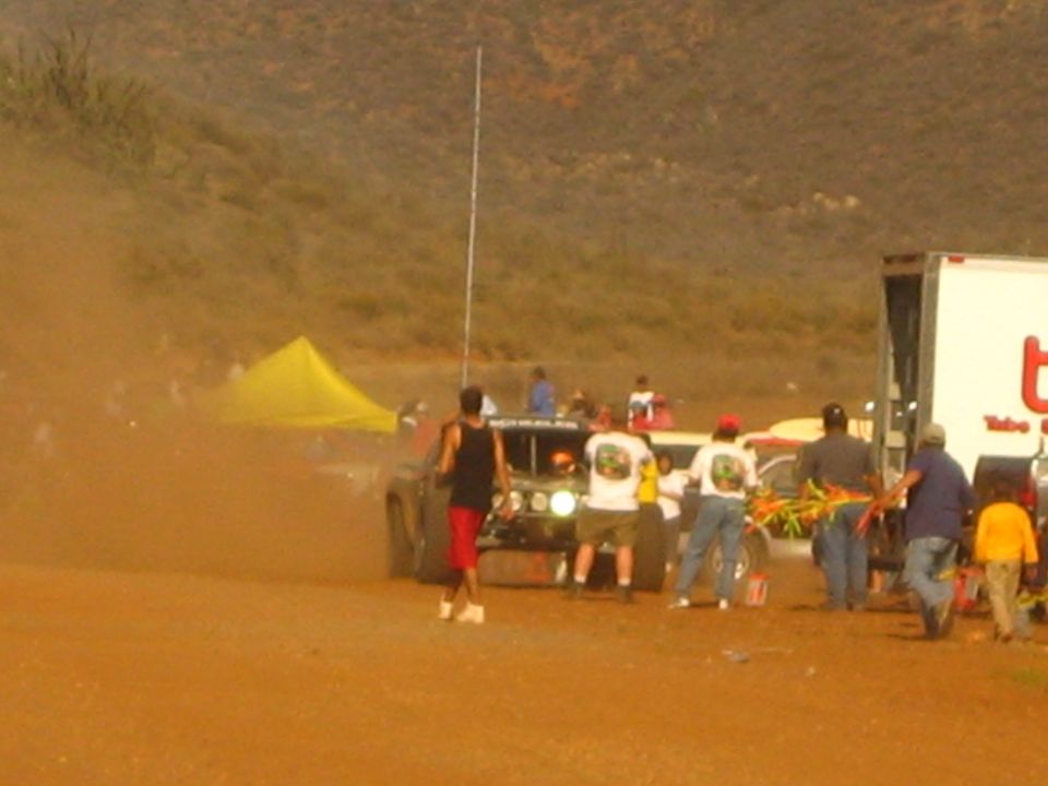 Off-road truck and spectators in red dust at a desert race pit