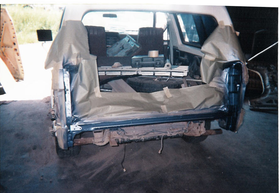 Rear of SUV body shell masked with paper and tape for paint, blue tailgate area exposed