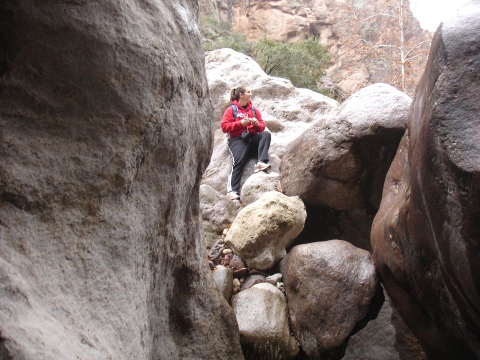 Woman in red hoodie and black pants stands on rocks in a canyon