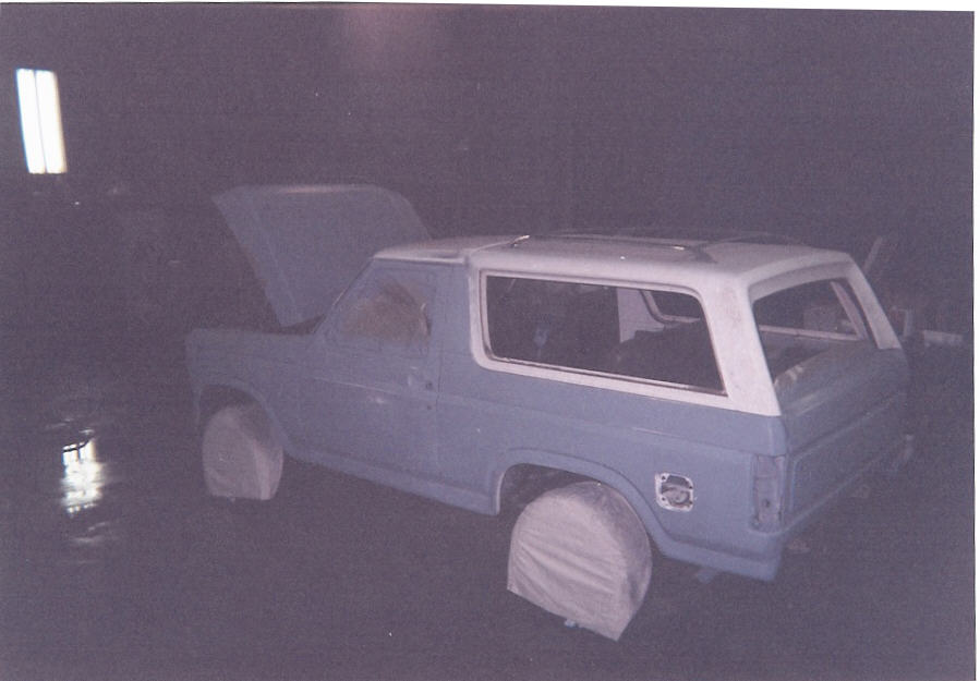 Light blue Ford Bronco SUV with white top and hood up in a dark garage