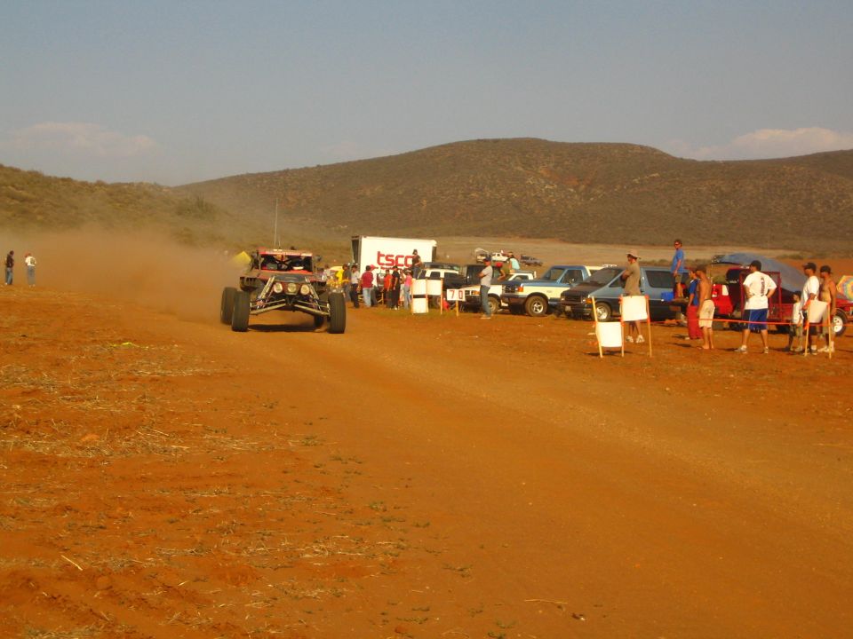 Desert race buggy approaching a line of spectators and trucks