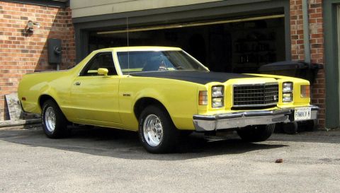1978 Ford Ranchero - This yellow coupe utility vehicle has a distinctive grille and a black hood, parked in front of a brick garage.