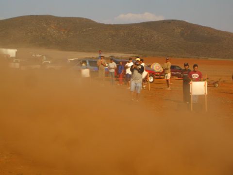 1990 Ford Bronco - Spectators and parked vehicles sit in a thick cloud of red dust along a desert race course.