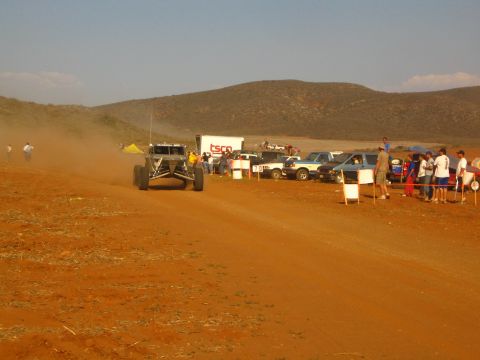 1990 Ford Bronco - off-road buggy speeds along a red dirt course past a TSCO box trailer and a line of spectators.