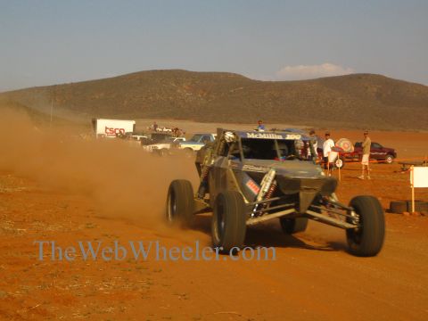 1990 Ford Bronco - off-road buggy races head-on through red dust past a McMillin 300 race banner.