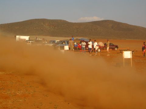 1990 Ford Bronco - line of spectators and parked vehicles stand behind a rolling wall of red desert dust.