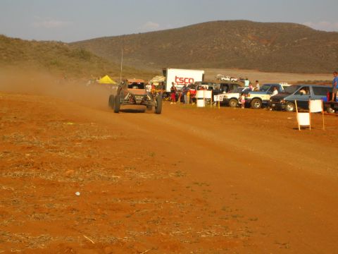 1990 Ford Bronco - off-road buggy raises dust on a red dirt course beside a TSCO trailer and a yellow canopy.