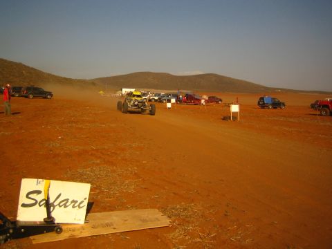 1990 Ford Bronco - off-road buggy races on a wide red dirt course beyond a hand-lettered Safari course sign.