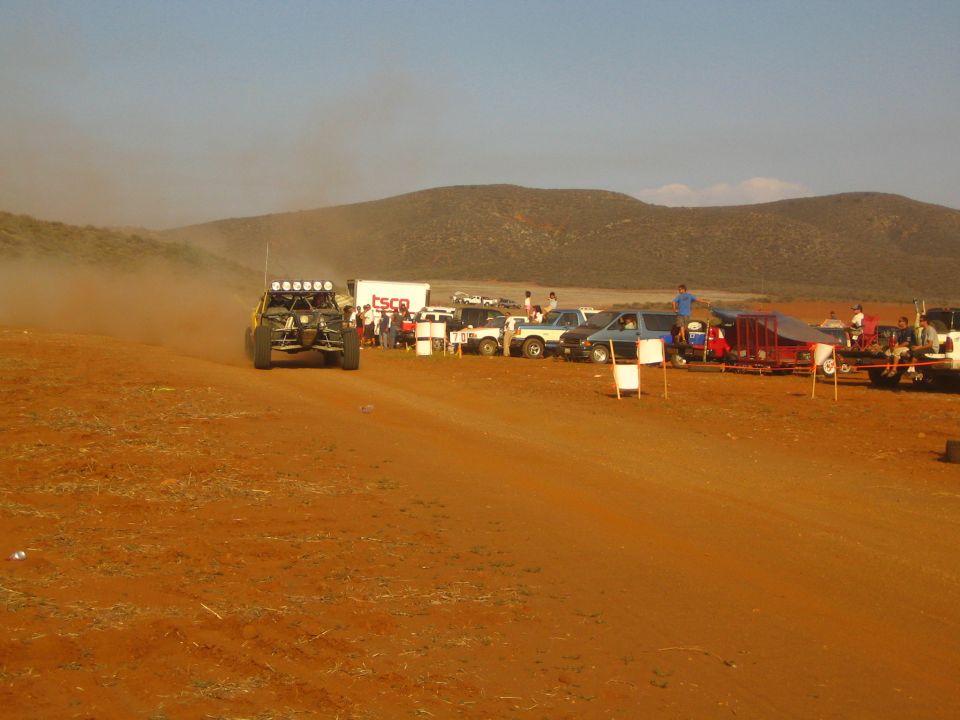 Dark off-road buggy with light bar driving away on red dirt course