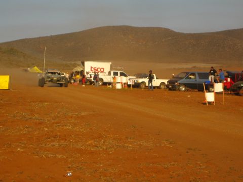 1990 Ford Bronco - off-road buggy trails dust past a TSCO box truck and a line of pickups along a red dirt course.