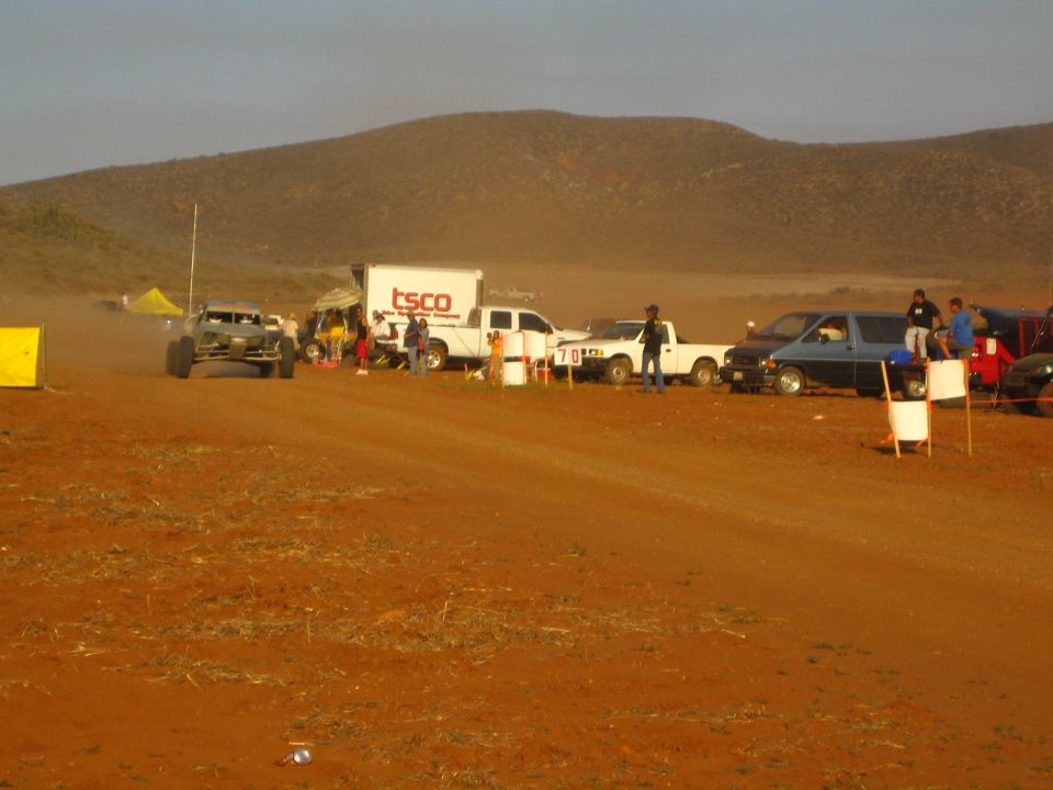 Off-road buggy passing TSCO box truck and pickups on dirt course