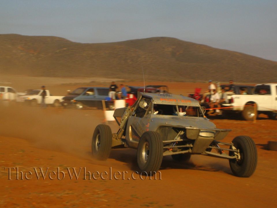 Gray tube-frame off-road buggy racing on red dirt at speed