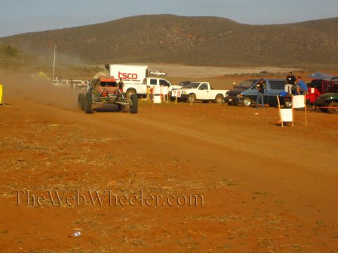 1990 Ford Bronco - off-road buggy trails dust along a red dirt course past a TSCO box truck and a row of pickups.