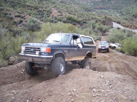 1991 Ford Bronco - A group of SUVs navigate a challenging off-road trail in a desert landscape.
