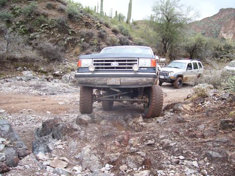 1991 Ford Bronco - A lifted 1991 Ford Bronco navigates a rocky off-road path, with a Jeep visible behind it.