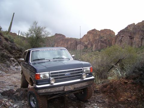 1991 Ford Bronco - 1991 Ford Bronco navigating a rough desert landscape with rocky terrain and sparse vegetation.