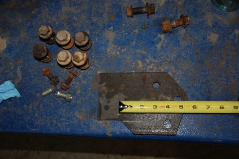 1996 Ford Bronco - A metal bracket and assorted bolts are laid out on a blue surface, with a tape measure indicating the bracket's size.