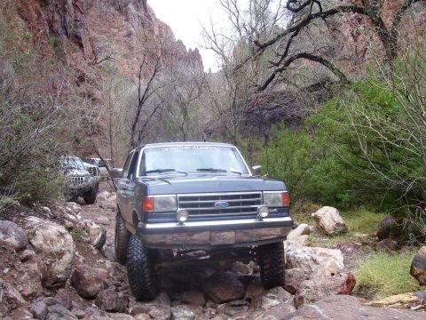 1991 Ford Bronco - Ford Bronco tackles a challenging off-road path in a scenic canyon environment.