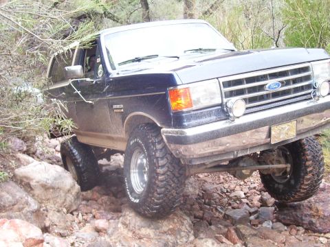 1991 Ford Bronco - A dark blue Ford Bronco navigates a rocky trail, demonstrating its off-road capabilities.