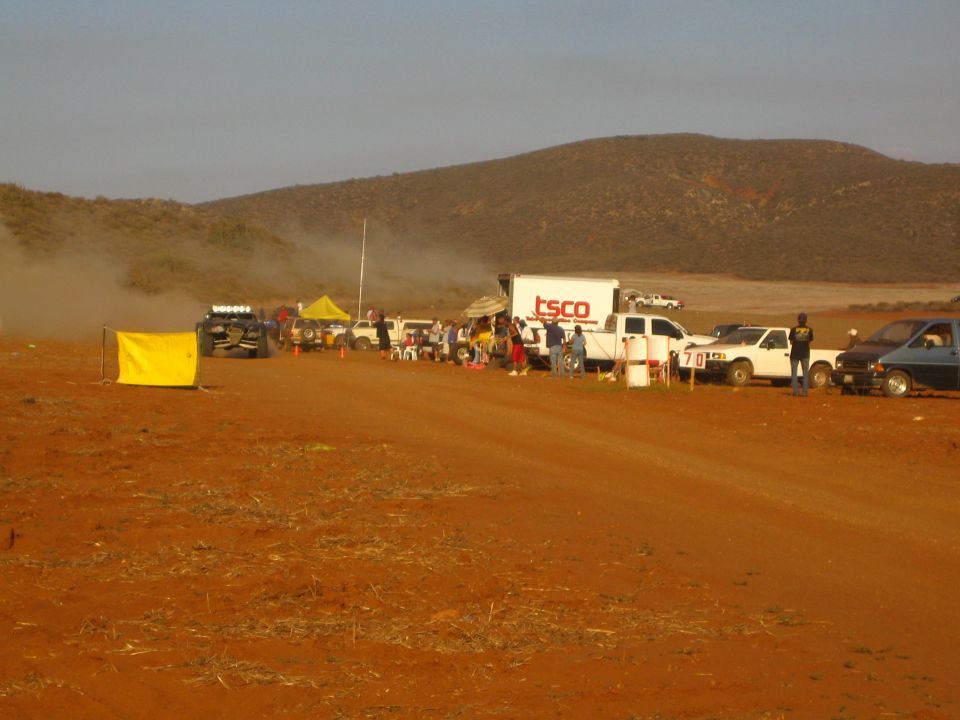 Dusty desert race pit with crowd, TSCO truck and parked pickups