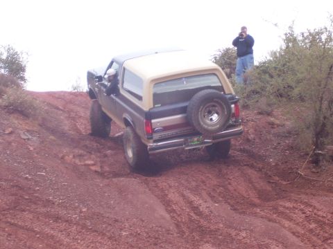 1991 Ford Bronco - A Ford Bronco navigates a steep, dusty incline with a photographer observing from the hillside.