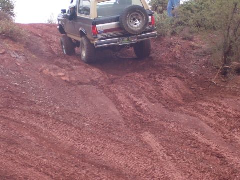 1991 Ford Bronco - A Ford Bronco navigates a steep, muddy incline in a dry, brushy environment.