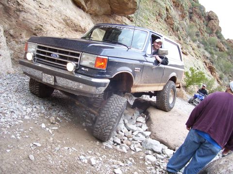 1991 Ford Bronco - A 1991 Ford Bronco tackles a challenging rocky terrain, with a driver and an ATV rider present.