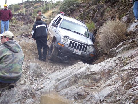1991 Ford Bronco - Jeep Liberty struggling on a difficult rocky trail, with onlookers present.