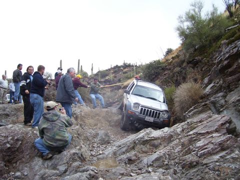1991 Ford Bronco - A group of people are helping to pull a Jeep Liberty out of a muddy, rocky ravine.
