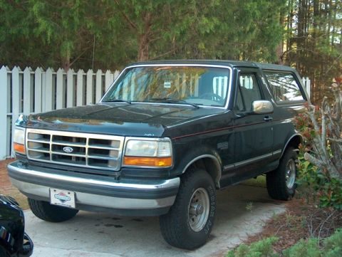 1992 Ford Bronco - A dark blue 1992 Ford Bronco is parked in a driveway with a white picket fence in the background.