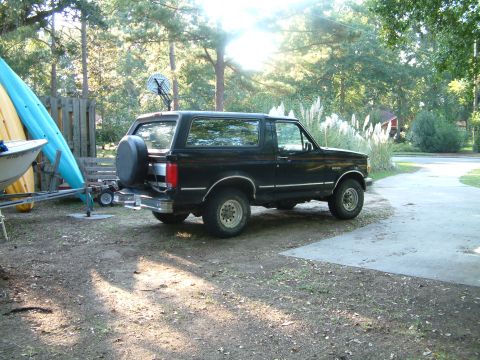 1992 Ford Bronco - This black 1992 Ford Bronco is parked on a driveway with kayaks and a boat trailer nearby.
