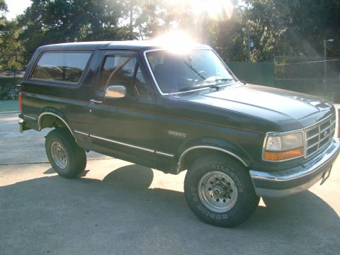 1992 Ford Bronco - A 1992 Ford Bronco is shown from the front three-quarter view, parked on a concrete surface with trees in the background.
