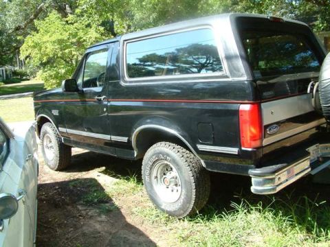 1992 Ford Bronco - This black Ford Bronco is parked outdoors on a sunny day, with trees and foliage in the background.