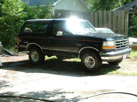 1992 Ford Bronco - A black 1992 Ford Bronco is parked outdoors, showing its side and front profile with a spare tire visible through the rear window.