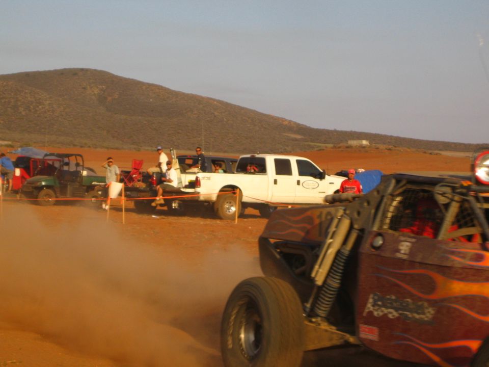 White crew-cab pickup at desert pit with flame-painted off-road buggy in foreground