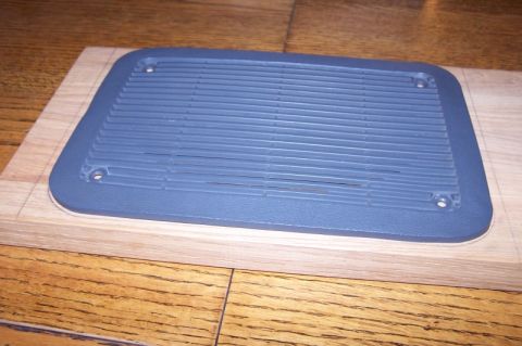 1990 Ford Bronco - A close-up view of a gray plastic speaker grille, possibly for a vehicle, resting on a wooden plank.
