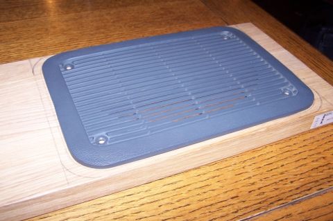 1990 Ford Bronco - A gray plastic speaker grille is shown on a wooden surface, possibly for installation.