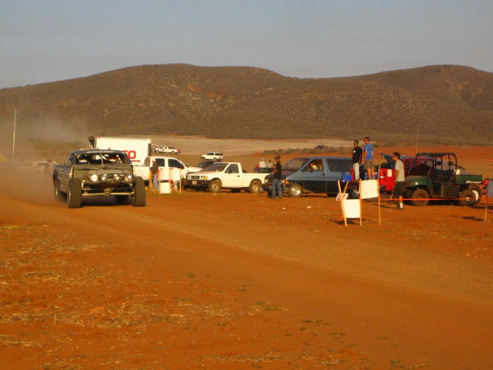 Off-road truck on red dirt course past TSCO truck, pickups and side-by-side