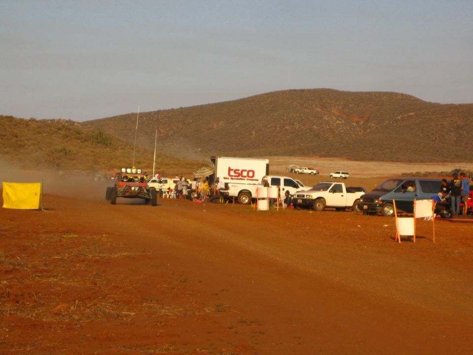 Off-road buggy with light bar passing pit vehicles and TSCO truck in desert