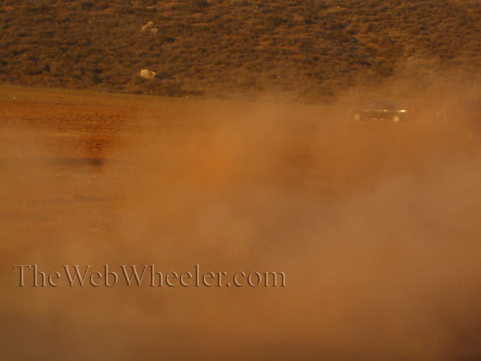 Distant vehicle on a desert hillside mostly obscured by a wall of dust
