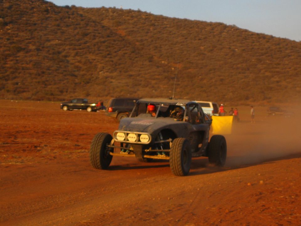 Two-seat off-road buggy raising dust on a desert track at golden hour