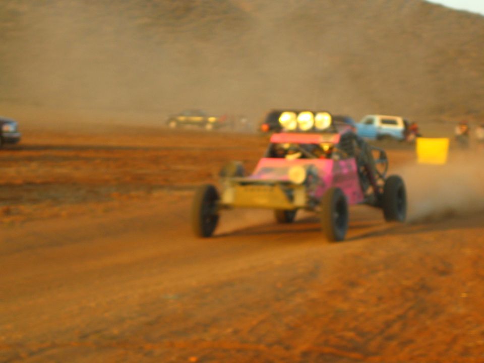 Pink and gold off-road buggy numbered 999 racing in dust on a desert track