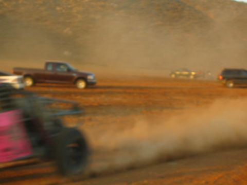 1990 Ford Bronco - motion-blurred desert race scene shows a maroon pickup and a partly visible off-road buggy amid clouds of dust.