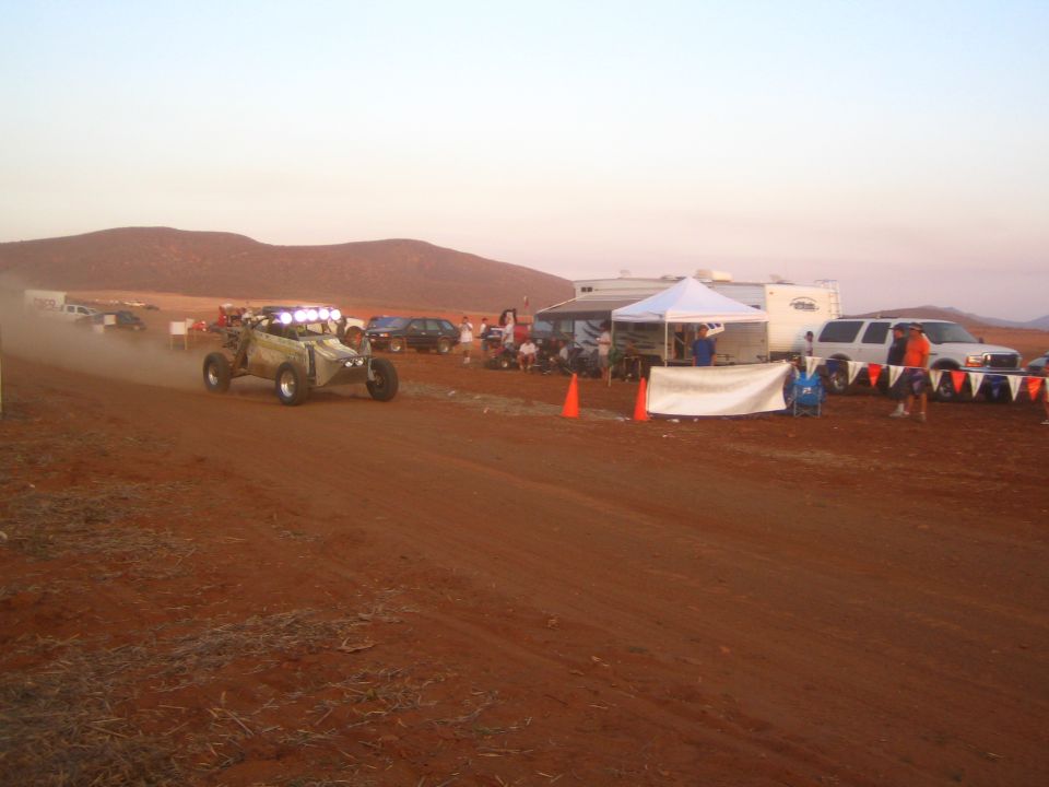 Off-road buggy with light bar on a desert track at dusk near a pit camp
