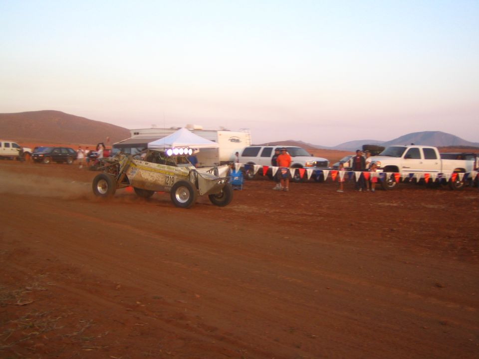 Tubular off-road race buggy racing on a desert dirt track at dusk