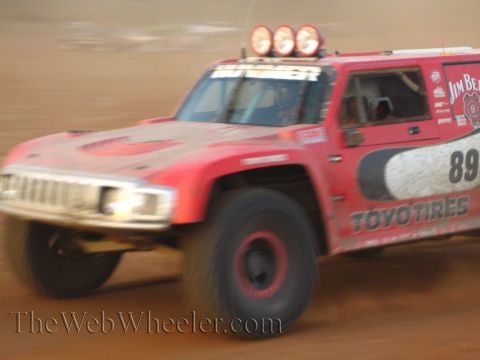 1990 Ford Bronco - red off-road race truck numbered 89 with Toyo Tires and Jim Beam livery races through the desert with motion blur.