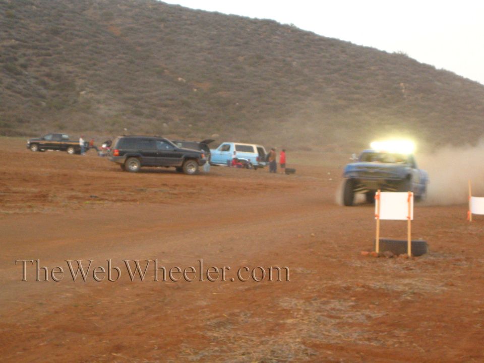 Blue off-road race truck with lit light bar on a desert course at dusk