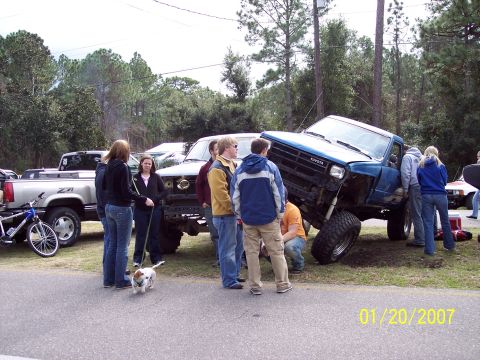 1984 Toyota 4Runner - A group of people examine a lifted blue Toyota pickup truck on a grassy area next to a road.